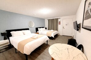 Habitación de hotel con dos camas, una mesa redonda, un escritorio, un espejo y un televisor.