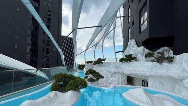 Ein moderner, innenliegender Pool mit einzigartigem Design, umgeben von künstlichem Schnee und Bäumen, neben einem Hochhaus.