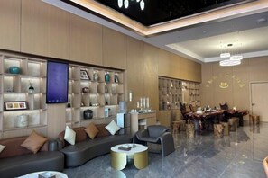 A modern hotel lobby with a seating area, a dining table, and a display of decorative items. - Boten Jinchi holiday Spa Hotel (Boten)