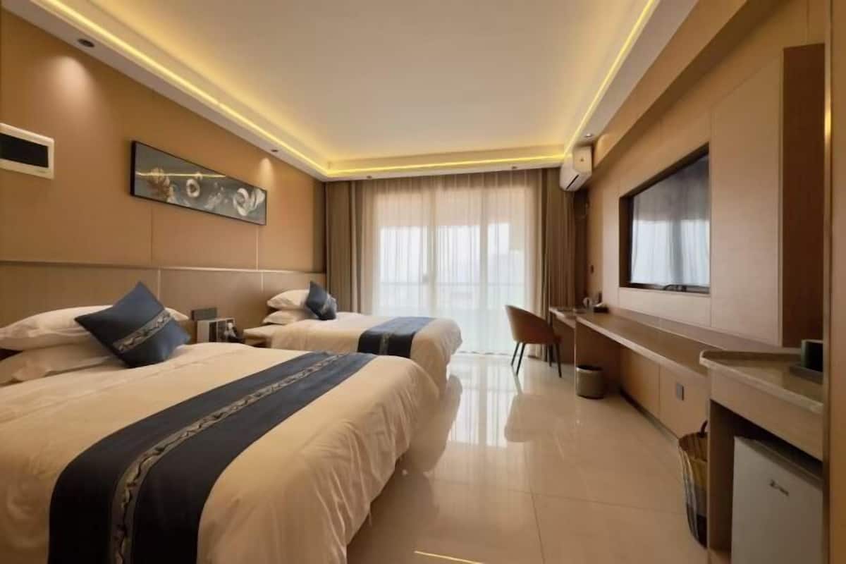 A hotel room with two beds, a desk, a chair, a TV, and a window with curtains.