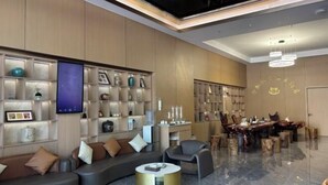 A modern living room with a sofa, armchairs, and a coffee table. There is a dining area with a wooden table and chairs. Shelves with decorative items line the walls. - Boten Jinchi holiday Spa Hotel (Boten)