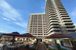 A high-rise hotel with multiple balconies, outdoor seating areas, and a clear sky. - Boten Jinchi holiday Spa Hotel (Boten)