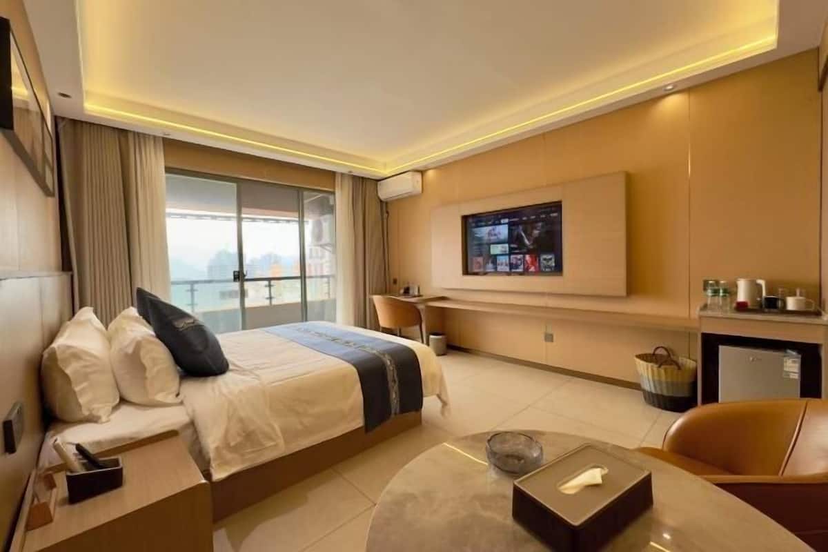 A hotel room with a bed, a desk, a TV, and a view of the city.