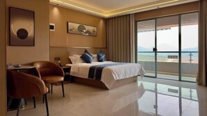 A modern hotel room with a bed, a desk, chairs, a large window with a view, and artwork on the walls. - Boten Jinchi holiday Spa Hotel (Boten)