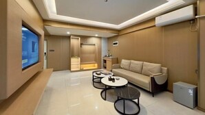 A modern living room with a sofa, two coffee tables, a flat-screen TV, and a small refrigerator. - Boten Jinchi holiday Spa Hotel (Boten)