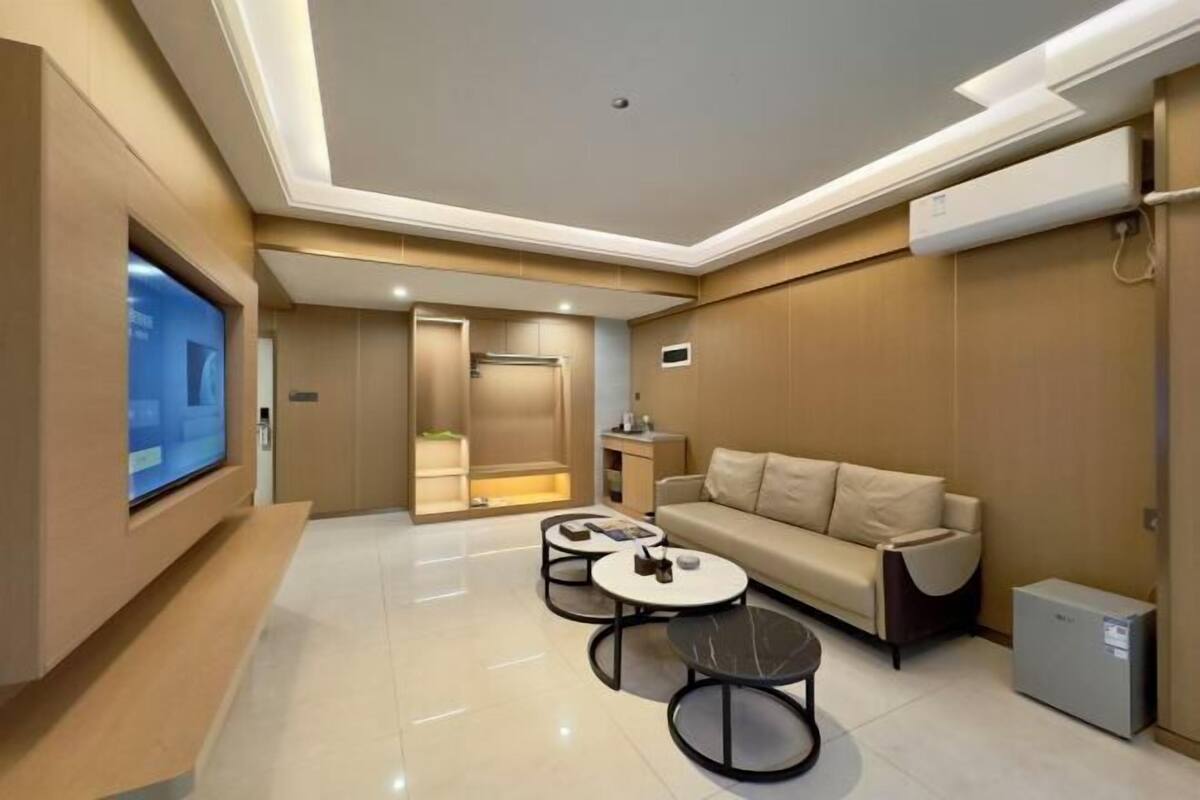 A modern living room with a sofa, two coffee tables, a flat-screen TV, and a small refrigerator.