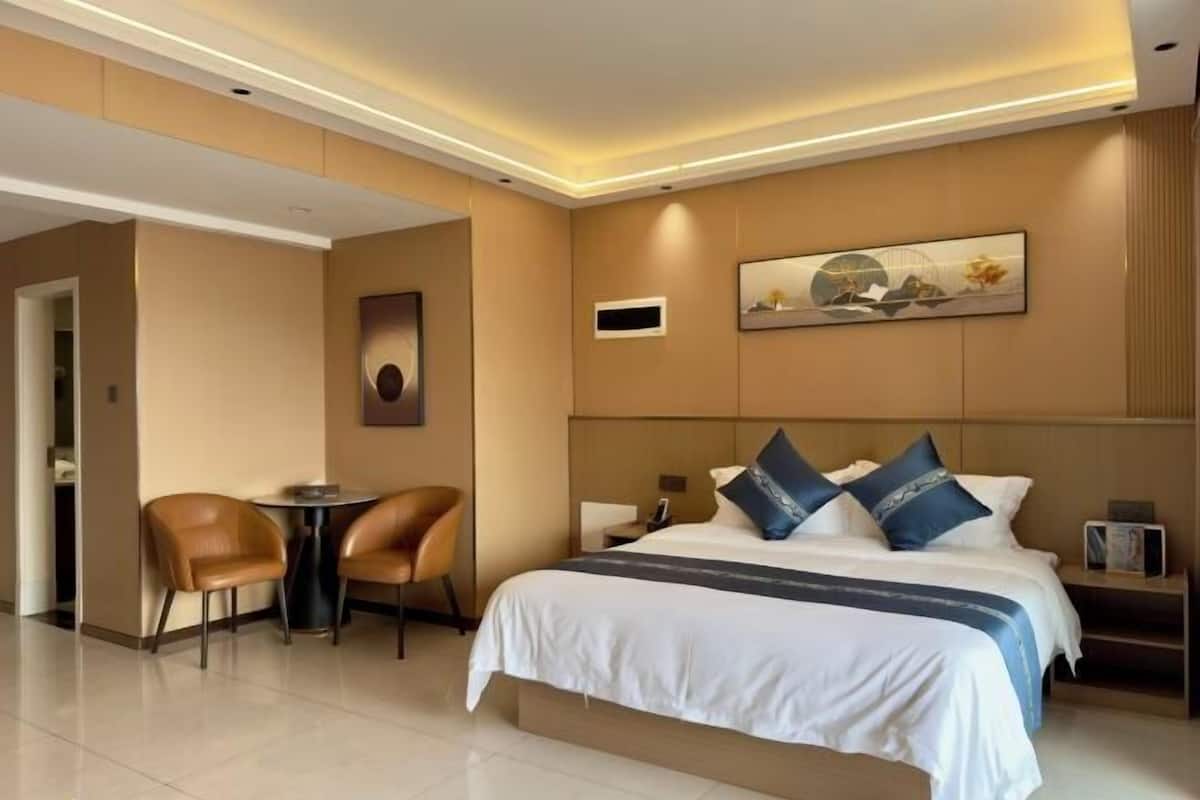 A hotel room with a bed, two chairs, a small table, and a wall-mounted artwork.