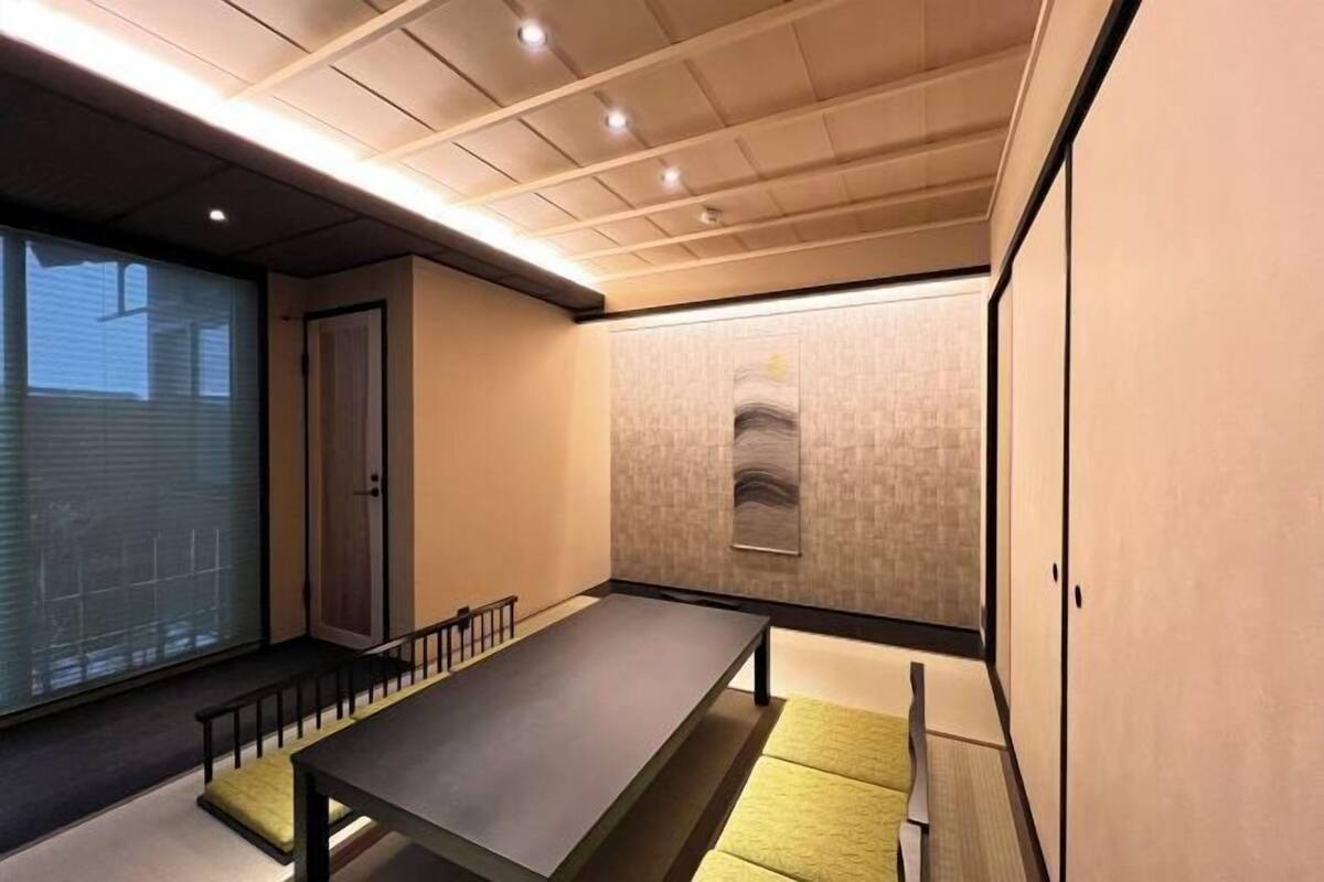 A room with a long table, a bench, a sliding door, and a wall-mounted artwork.