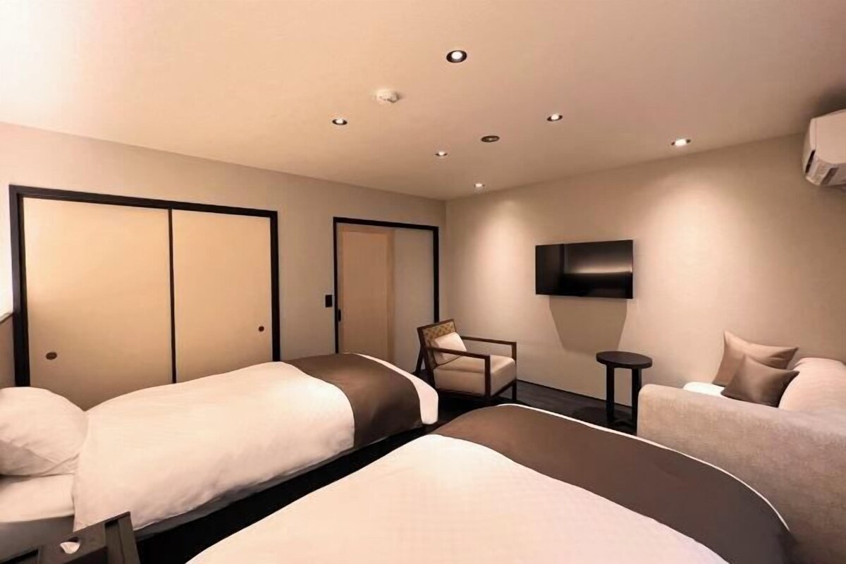 Une chambre d’hôtel avec deux lits, une chaise, une petite table et un téléviseur fixé au mur.