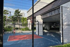 Una cancha de baloncesto al aire libre con recinto de malla, rodeada de árboles y edificios.