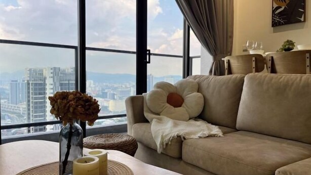 A modern living room with a large window, a beige sofa, a vase with dried flowers, and a wooden table with candles.