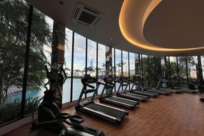 Un gimnasio con cintas de correr y equipo de ejercicio, ventanas amplias y vista a un cuerpo de agua.