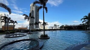 A swimming pool with multiple water features, palm trees, and modern buildings in the background.
