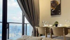 A modern living room with a sofa, a dining table with chairs, a potted plant, and a city view through large windows.