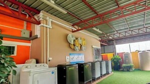 A laundry area with a washing machine and several dryers, a green artificial turf floor, and a wall with decorative plates. - leader residences (Bang Phli)