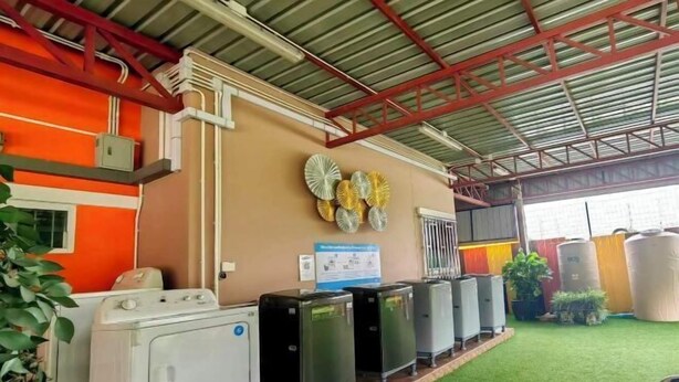 A laundry area with a washing machine and several dryers, a green artificial turf floor, and a wall with decorative plates. - leader residences (Bang Phli)