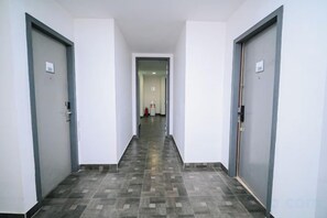 Un couloir avec deux portes de chaque côté, un sol carrelé et un mur de couleur claire.