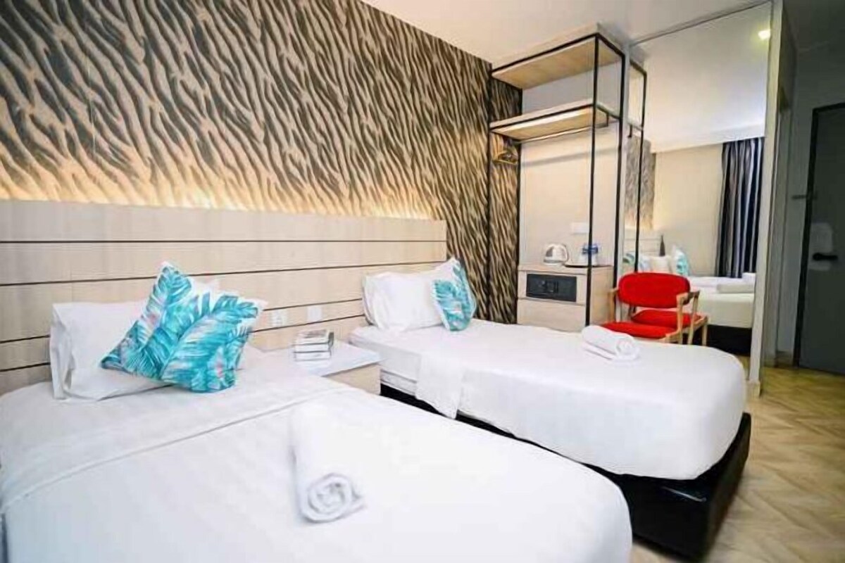 A hotel room with two beds, a mirror, a red chair, and a wooden wall.