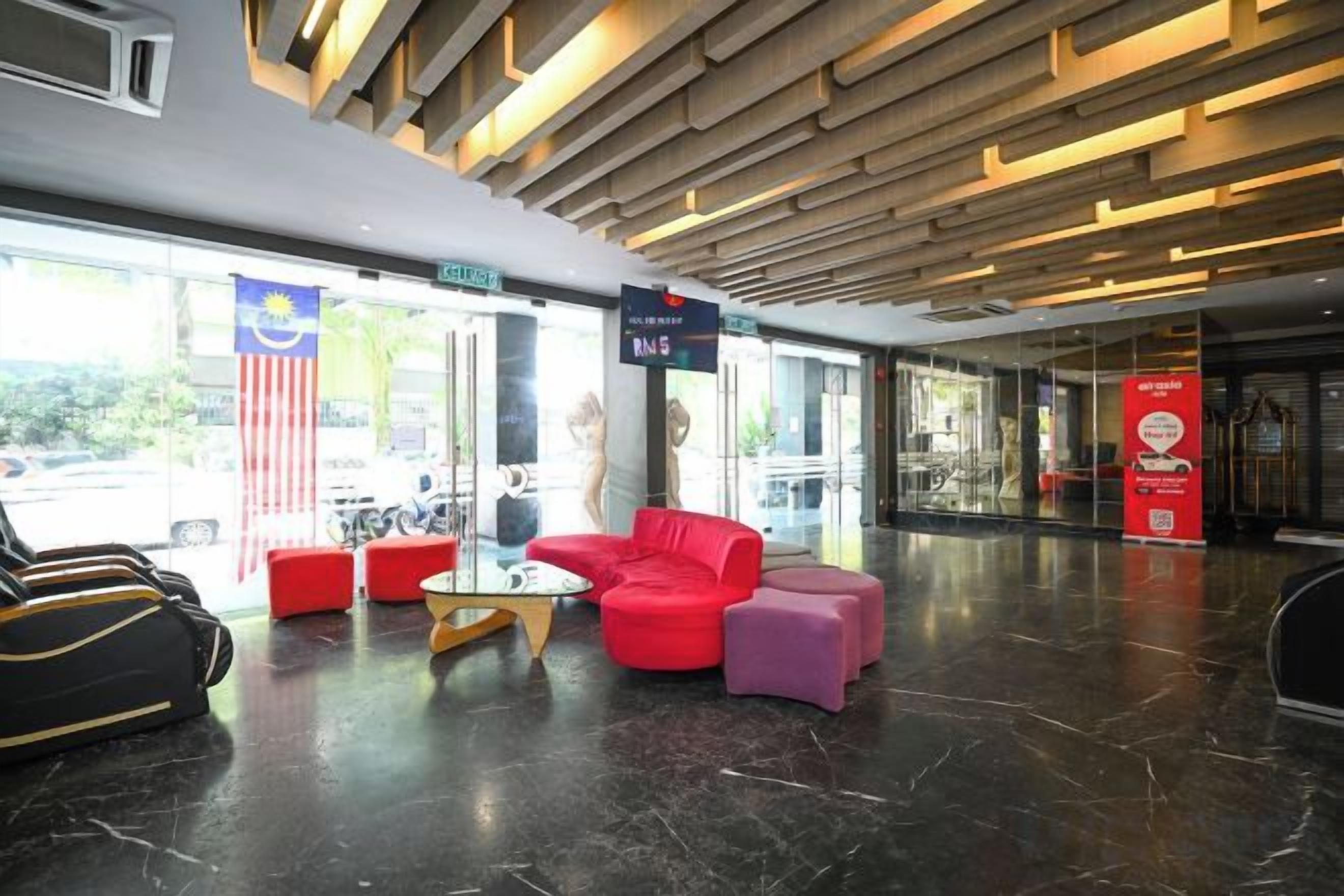 A hotel lobby with a reception desk, seating area with red and purple sofas, and a glass wall offering a view of the street.