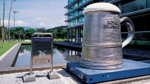 A large metal mug with "ROYAL BALANCE" engraved on it, placed on a platform with a sign next to it. - Kingston Hotel 2 @ Setapak (Kuala Lumpur)