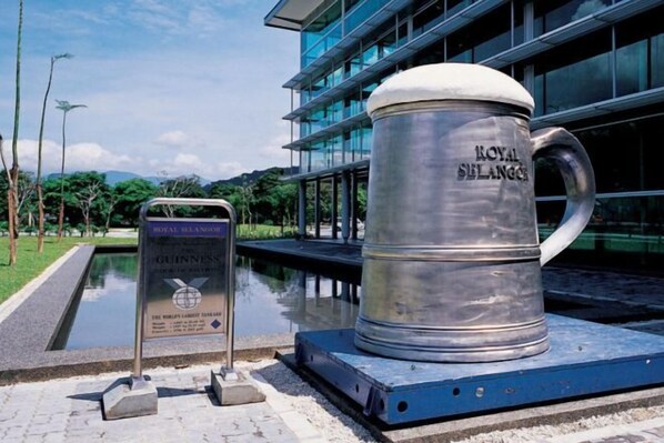 A large metal mug with "ROYAL BALANCE" engraved on it, placed on a platform with a sign next to it. - Kingston Hotel 2 @ Setapak (Kuala Lumpur)