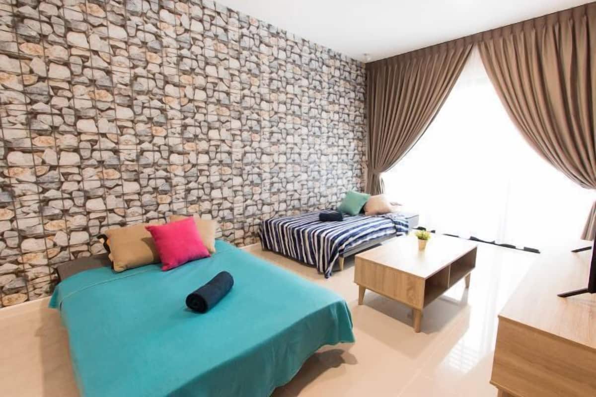 A room with a stone wall, a bed with teal bedding, a striped sofa, a wooden table, and a window with curtains.