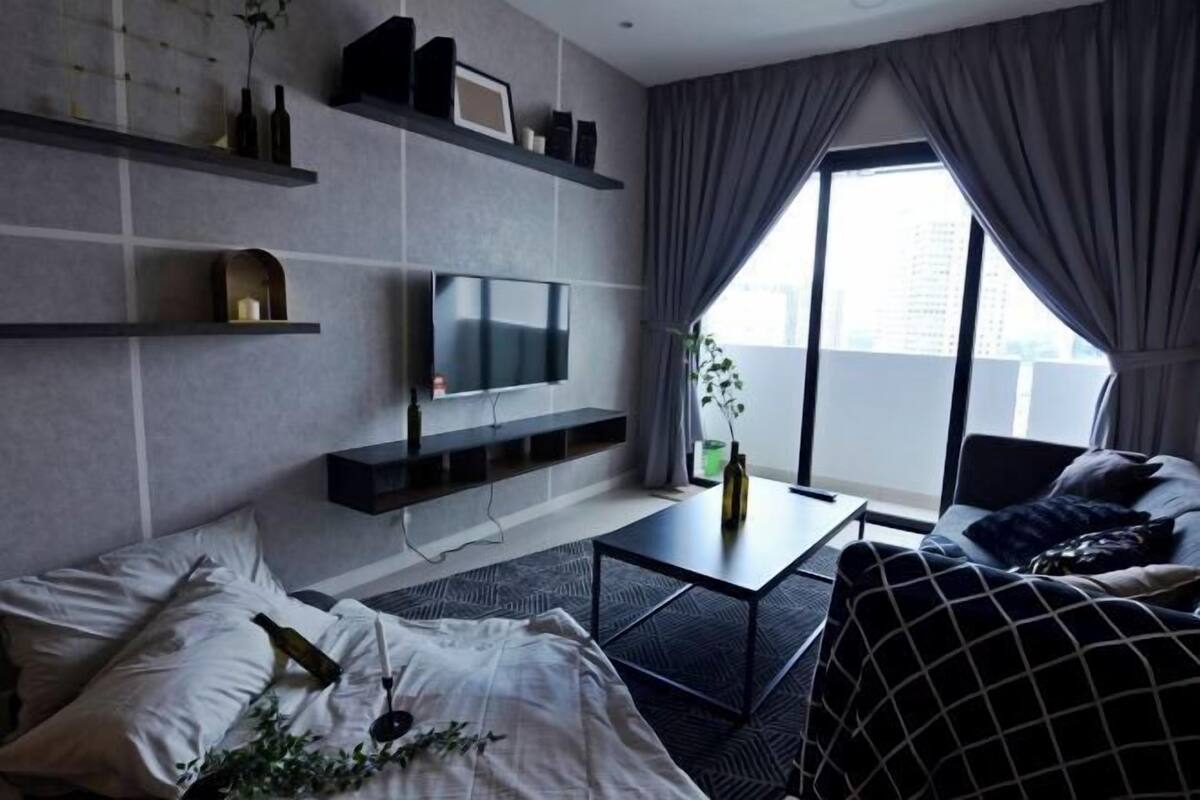 A modern living room with a sofa, a coffee table, a TV mounted on the wall, and a balcony with curtains.
