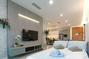 Un dormitorio moderno con televisión de pantalla plana, una cama con almohadas, una mesita de noche y una planta pequeña.