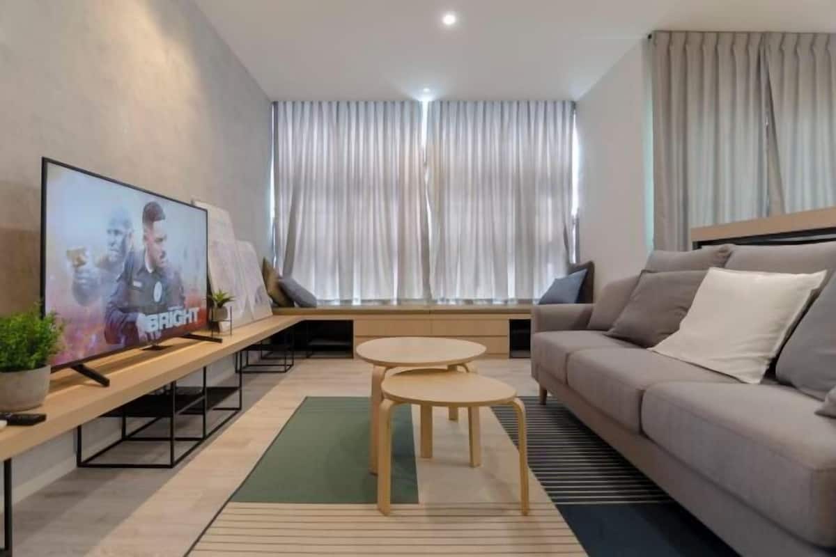 A modern living room with a sofa, two small round tables, a TV on a stand, and a large window with curtains.