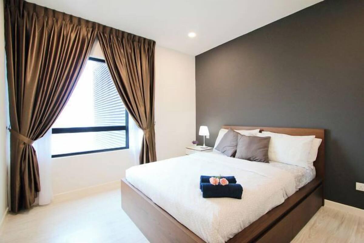 A bedroom with a large bed, a nightstand, a lamp, and a window with curtains.