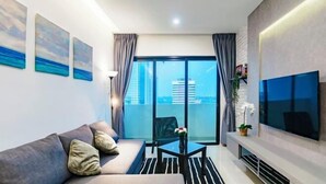 Una sala moderna con un sofá, una mesita, un televisor y un balcón con vistas a la ciudad.