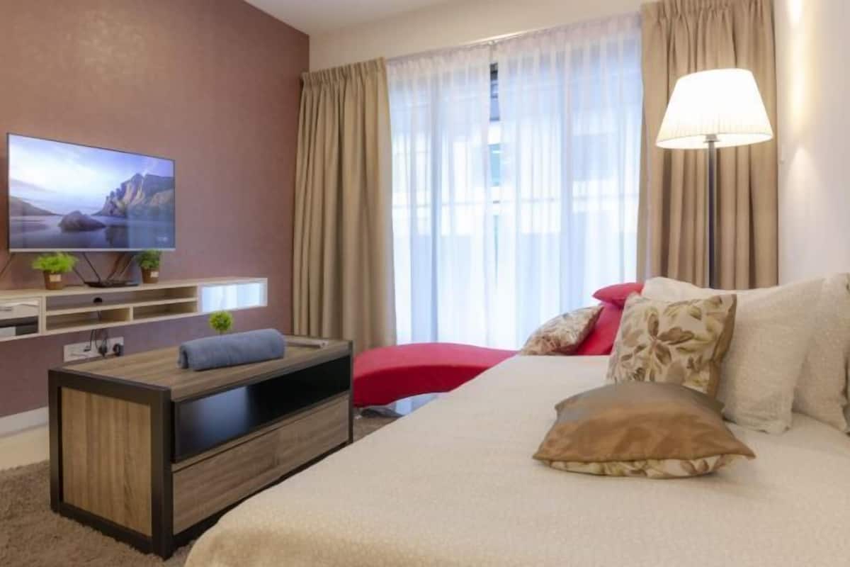 A modern hotel room with a large bed, a flat-screen TV mounted on a wooden console, a red chair, and a large window with curtains.