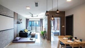 Una sala moderna con un sofá, una mesa de comedor para dos personas y un gran ventanal con cortinas.