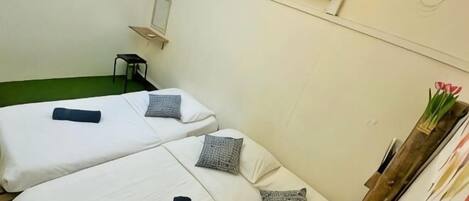 A room with two beds, a small table, and a chair. There is a wall-mounted air conditioner and a mirror.