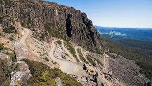 Une route de montagne sinueuse, bordée de falaises rocheuses et d’une végétation clairsemée.
