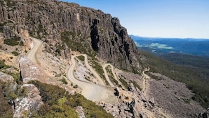 Een kronkelende bergweg met rotsachtige kliffen en schaarse begroeiing.