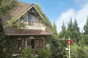 Une maison avec un toit à forte pente, une cheminée bien visible et une véranda dotée d’une balustrade.
