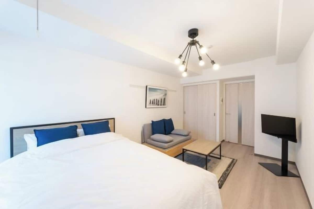 A modern hotel room with a large bed, a sofa, a TV, and a ceiling light fixture.