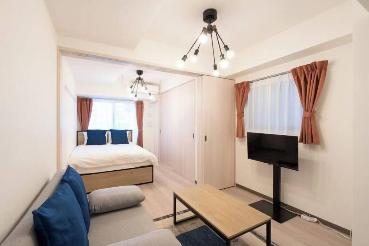A compact hotel room with a bed, a TV, a small table, and a sofa.