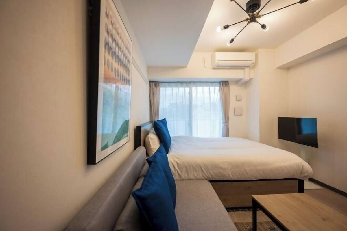 A hotel room with a bed, a sofa, a TV, and an air conditioning unit.