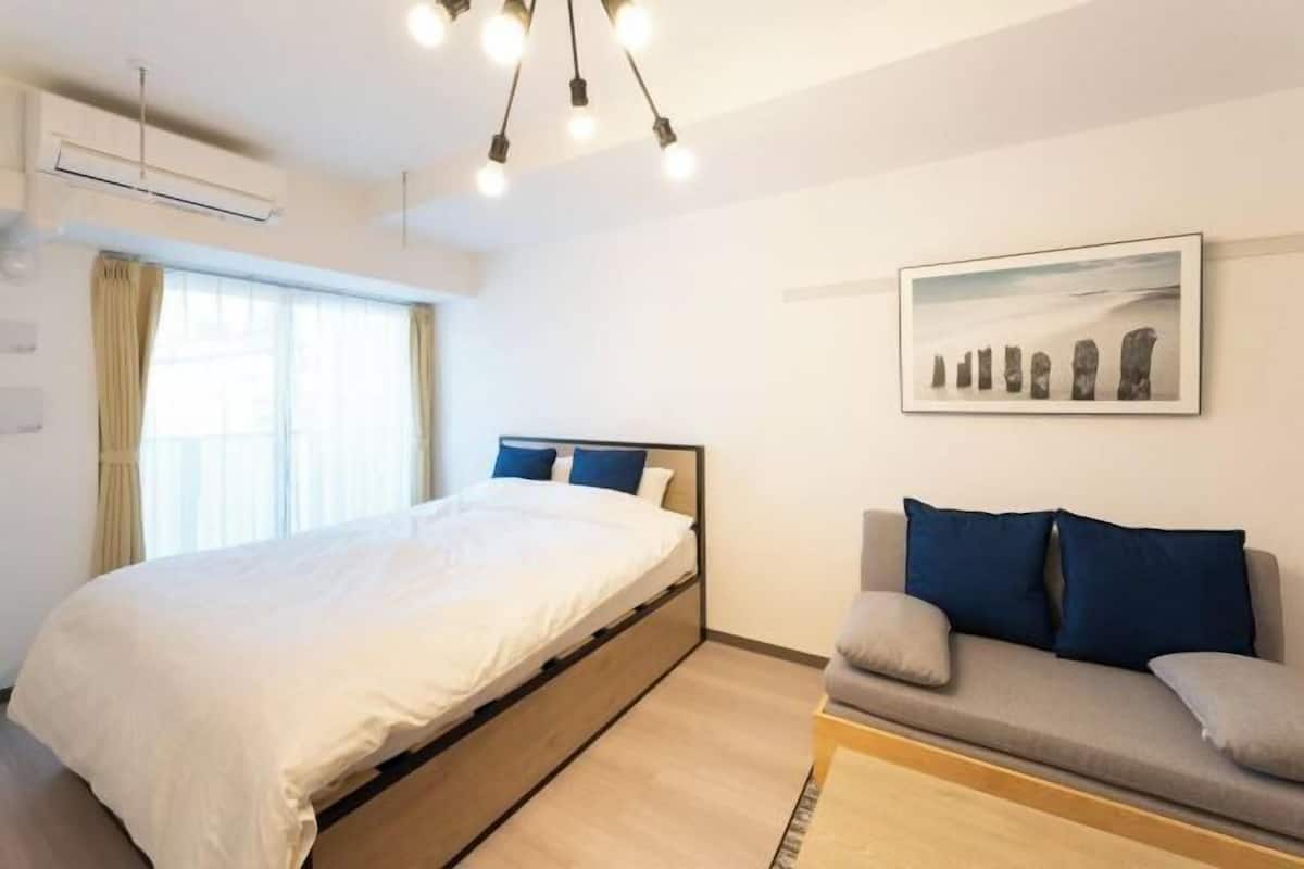 A bedroom with a bed, a sofa, a painting, and a window with curtains.