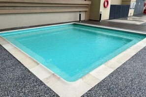Une piscine rectangulaire dont le bord est recouvert de carrelage, entourée d’une terrasse en béton.