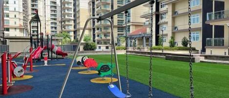Un parque infantil con columpios y toboganes, rodeado de edificios de apartamentos.