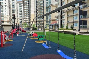 A playground with swings and slides, surrounded by apartment buildings. - LoFF Suite River View 2 Bedroom at Riverine Diamond Resort (Kuching)