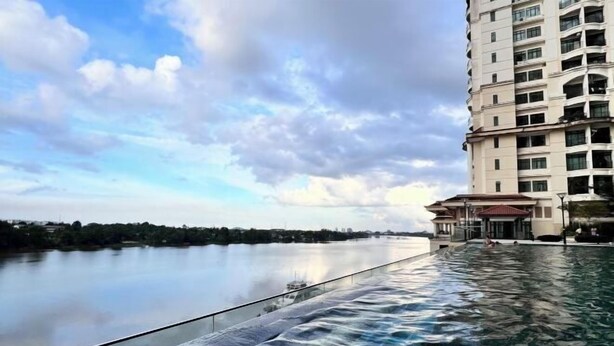 Een hotel met een zwembad met uitzicht op een kalme waterpartij, een heldere lucht en een veraf gelegen stadsgezicht.