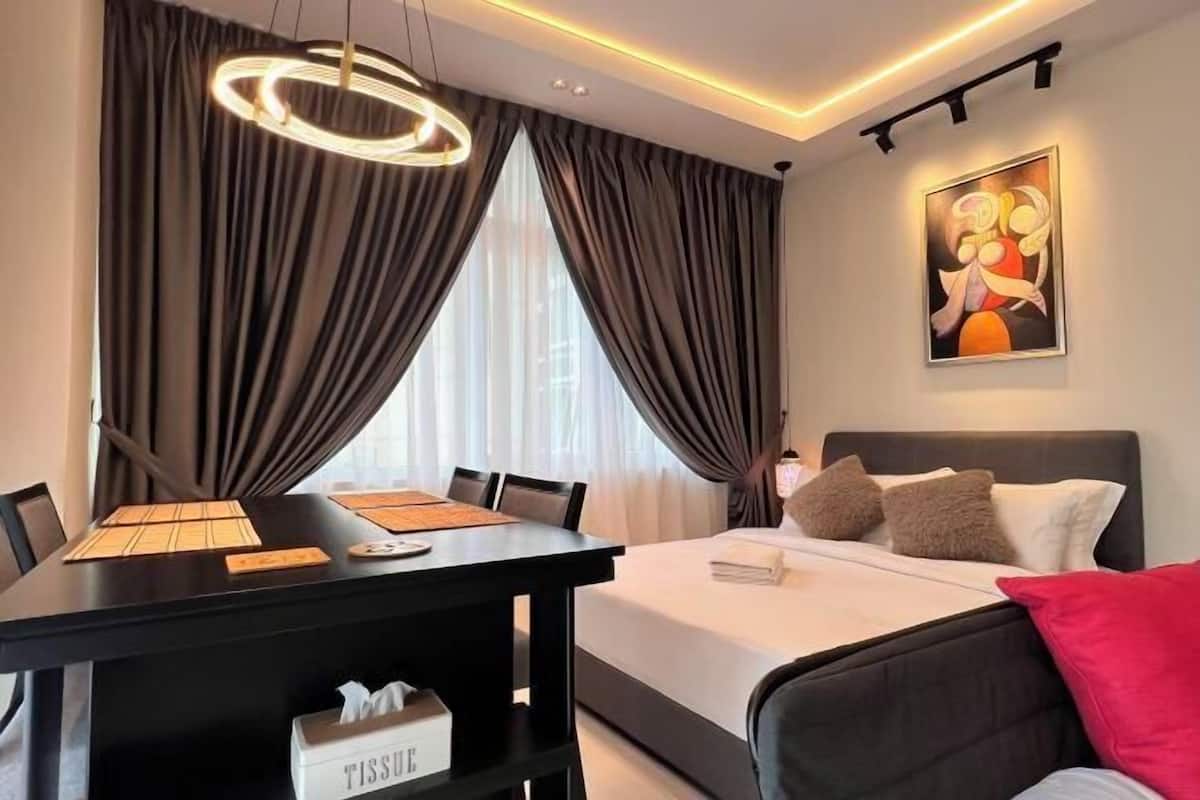 A modern hotel room with a bed, a dining table with chairs, a chandelier, and a painting on the wall.