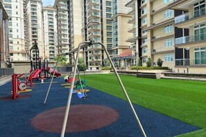 A playground with swings and slides, surrounded by a well-maintained lawn and residential buildings in the background. - LoFF Suite River View 2 Bedroom at Riverine Diamond Resort (Kuching)
