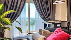Een moderne woonkamer met een bank, een eettafel en uitzicht op een waterpartij door grote ramen.