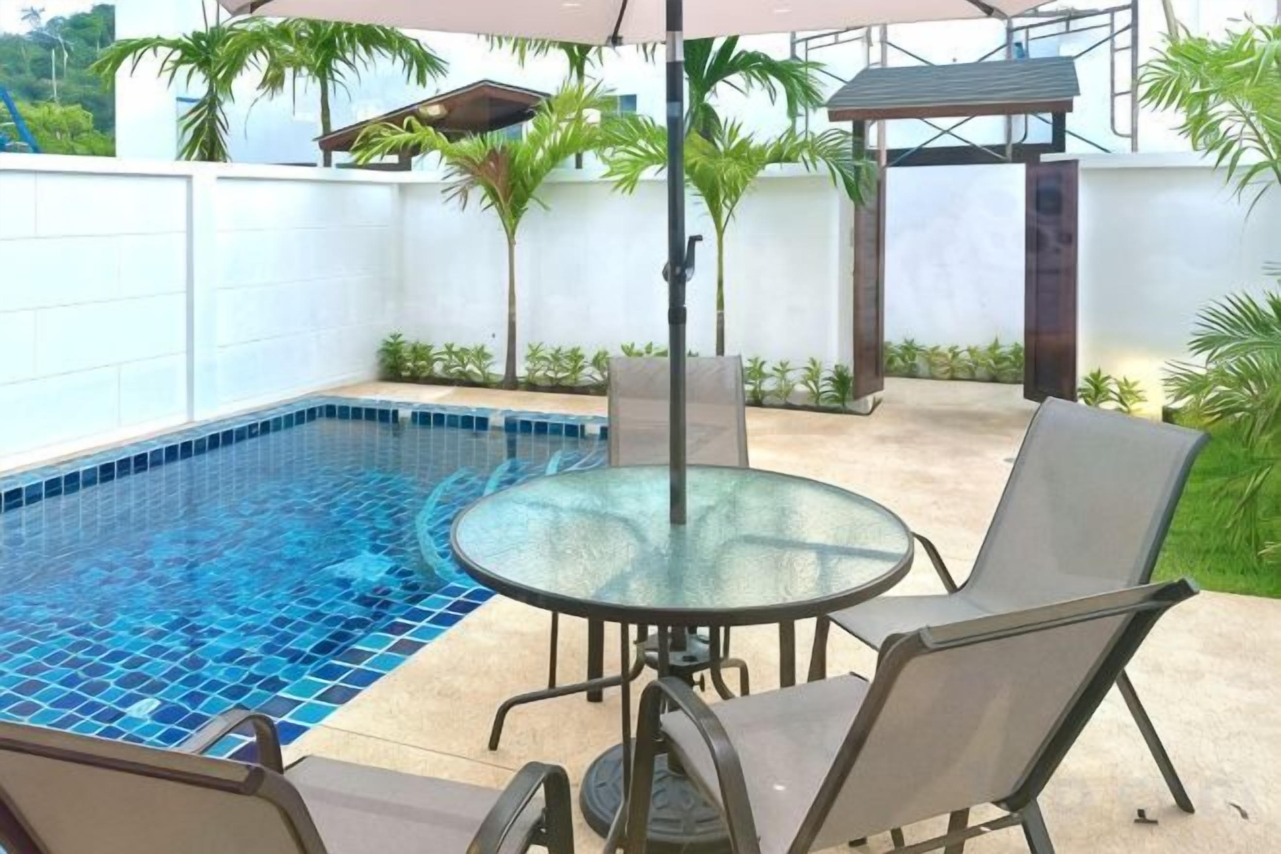 A swimming pool with a glass table and chairs, surrounded by a white wall and palm trees.