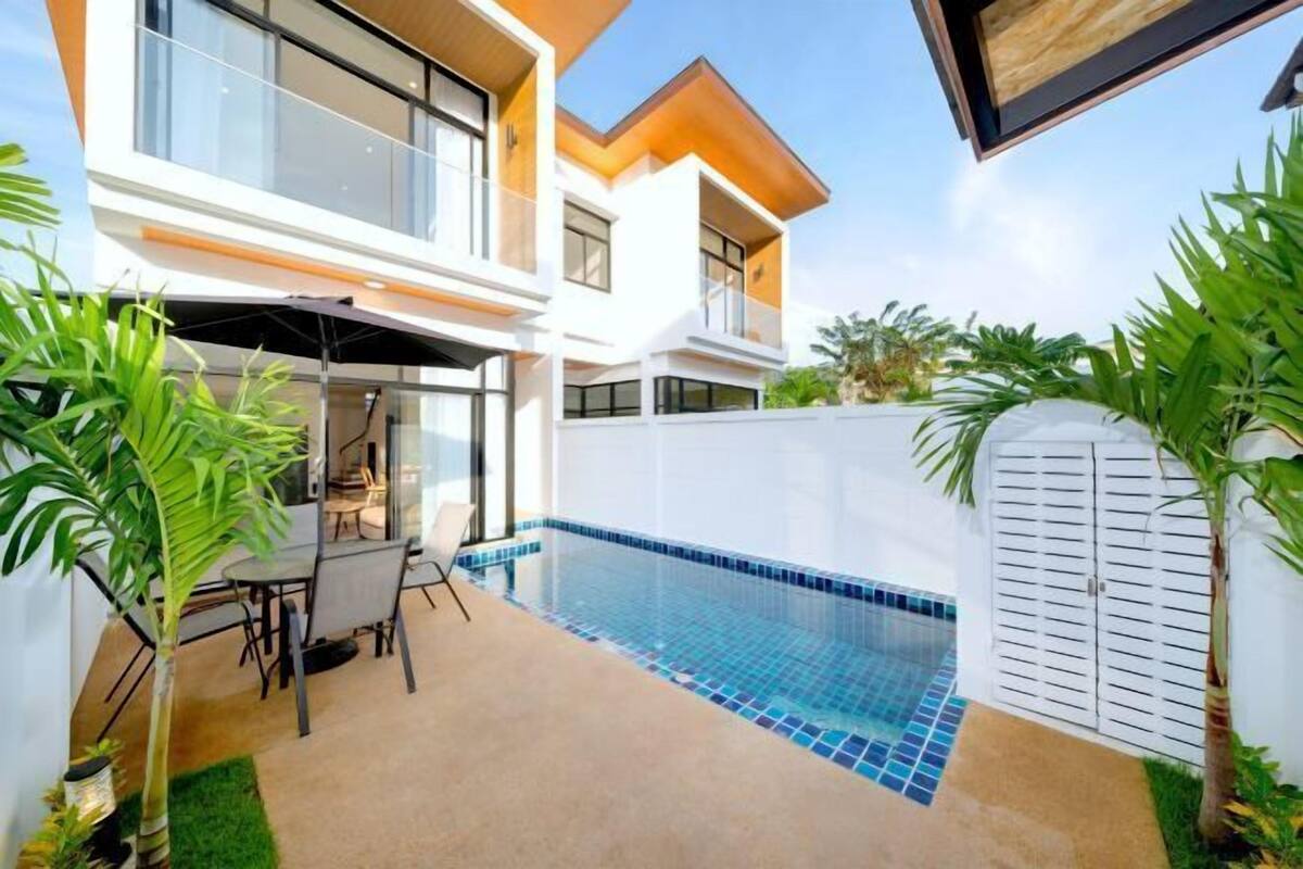 Een modern huis met een zwembad, een terras met tuinmeubels en een witte hek.
